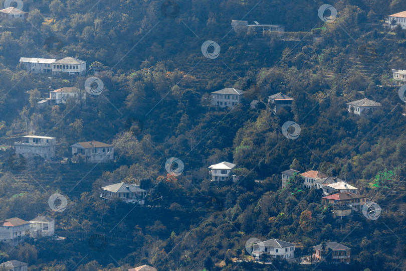 Скачать Сельская местность в Батуми. Сельские дома расположены на склонах гор. Одноэтажные, двухэтажные и трехэтажные дома окружены высокими зелеными деревьями. фотосток Ozero