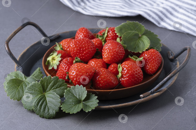 Скачать Свежесобранная клубника аккуратно разложена на коричневой деревянной тарелке, а рядом - зеленые листья фотосток Ozero