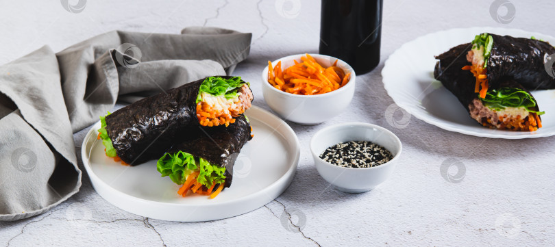 Скачать Тунец, сыр, корейская морковь и листья салата, завернутые в нори, на тарелке на веб-баннере "Стол" фотосток Ozero