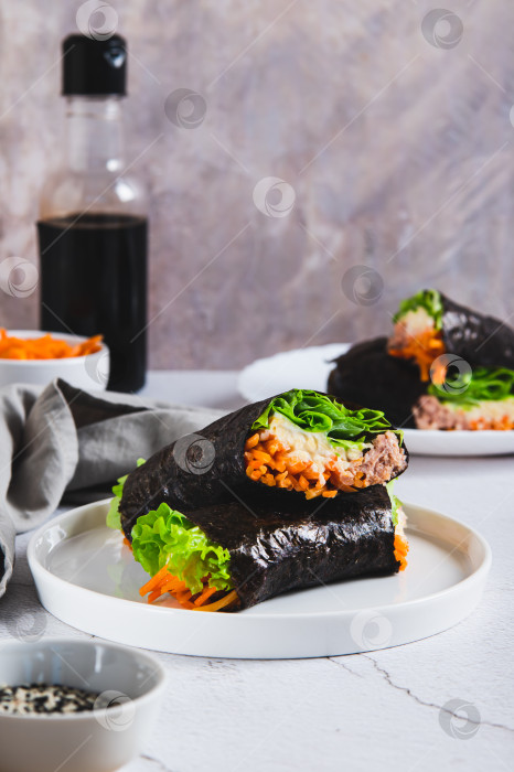 Скачать Тунец, сыр, корейская морковь и листья салата, завернутые в нори, на тарелке на столе, вид сверху фотосток Ozero