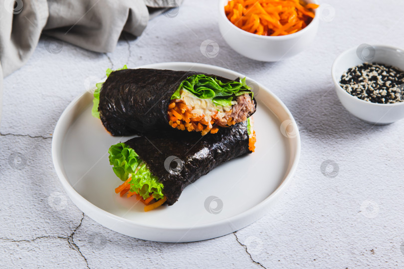 Скачать Роллы с тунцом, корейской морковью, листьями салата и соусом на тарелке на столе фотосток Ozero