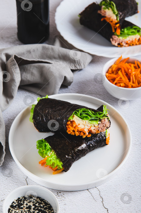 Скачать Роллы с тунцом, корейской морковью, листьями салата и соусом на тарелке на столе в вертикальном положении фотосток Ozero