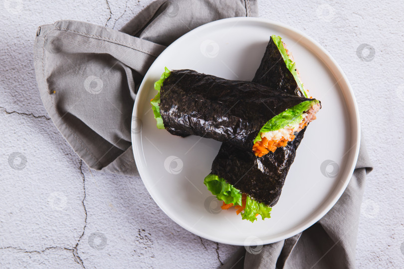 Скачать Крупный план тунца, сыра, корейской моркови и листьев салата, завернутых в нори, на тарелке, вид сверху фотосток Ozero