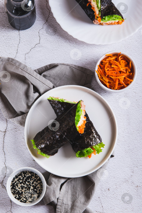 Скачать Роллы с тунцом, корейской морковью, листьями салата и соусом на тарелке, установленной на столешнице в вертикальном положении фотосток Ozero