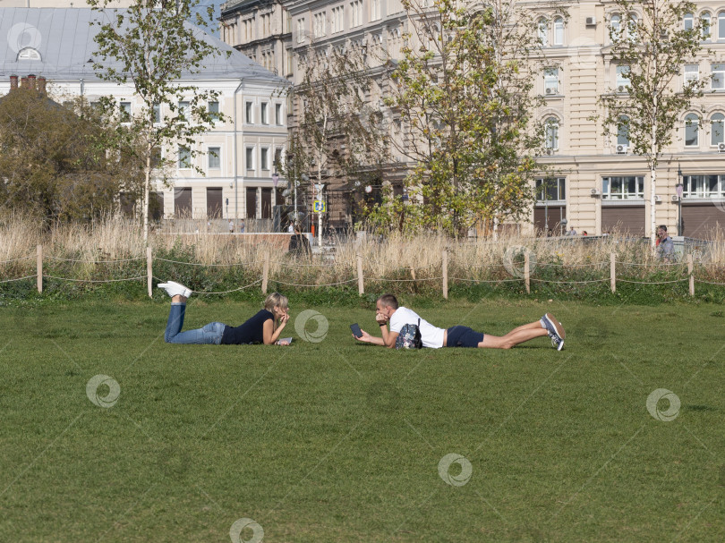 Скачать МОСКВА, РОССИЯ- 25 августа 2018 г.: Влюбленная пара лежит на траве рядом друг с другом, глядя в глаза фотосток Ozero