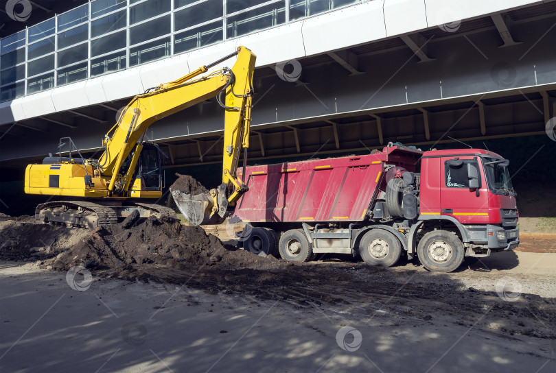 Скачать Экскаватор загружает грунт в кузов самосвала фотосток Ozero