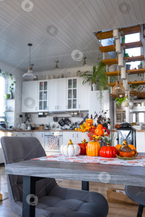 Скачать Декор белой классической кухни с тыквами, гирляндами, осенним букетом из желтых листьев к Хэллоуину и сбору урожая. Осеннее настроение в домашнем интерьере, современный стиль лофт. недвижимость, страхование, ипотека фотосток Ozero
