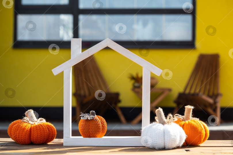 Скачать Осенний декор на крыльце желтого дома в виде тыквы, фонаря, гирлянд и фигурки крошечного домика и ключа. Вечеринка в честь Хэллоуина, осеннее настроение, праздник урожая, недвижимость, страхование, ипотека фотосток Ozero