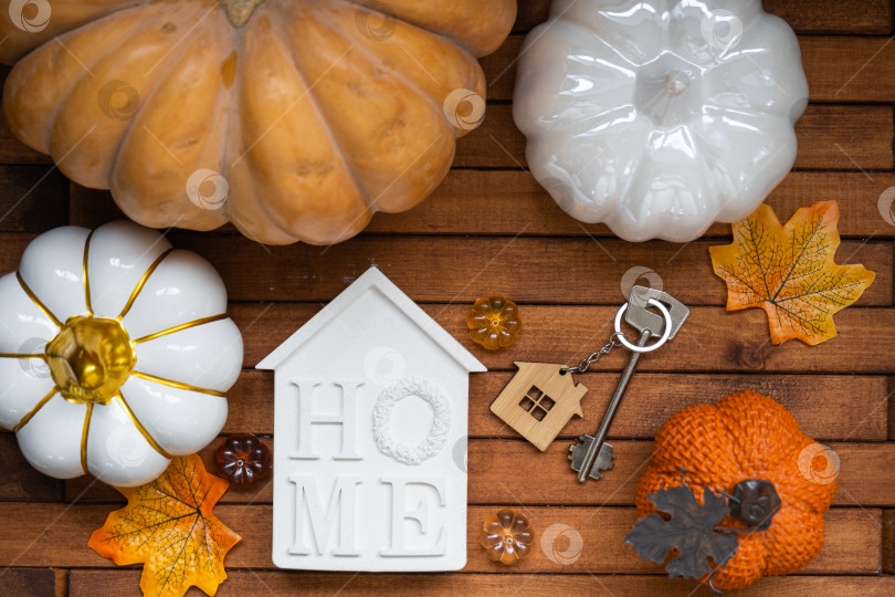 Скачать Уютный макет на деревянном фоне из реек с тыквами, осенними листьями, крошечным домиком и ключами - осеннее настроение, Хэллоуин, жилье, переезд, ипотека, страховка. фотосток Ozero