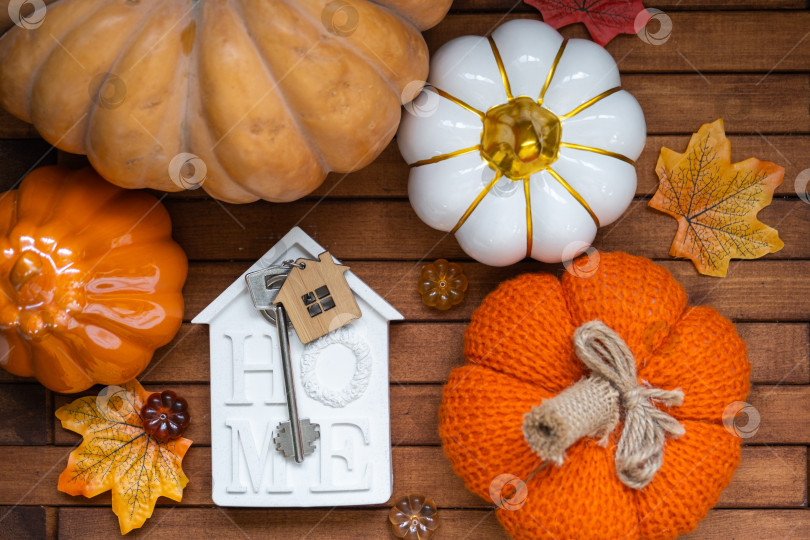 Скачать Уютный макет на деревянном фоне из реек с тыквами, осенними листьями, крошечным домиком и ключами - осеннее настроение, Хэллоуин, жилье, переезд, ипотека, страховка. фотосток Ozero