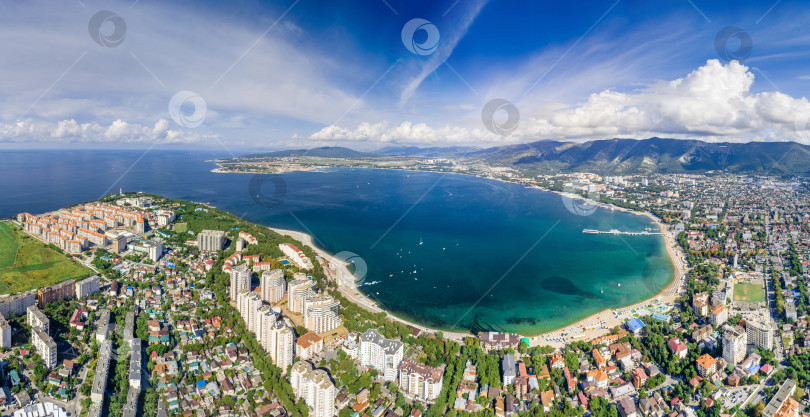 Скачать Панорама Геленджика с воздуха. Геленджикская бухта с голубой водой. Пляж вдоль берега бухты. Яхты на воде. Жилые дома вокруг бухты. Кавказские горы в белых облаках. фотосток Ozero