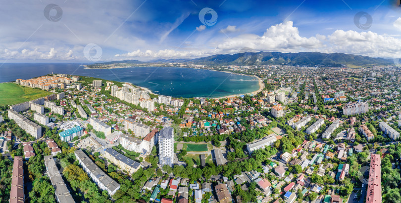 Скачать Панорама Геленджика с воздуха. Геленджикская бухта с голубой водой. Пляж вдоль берега бухты. Яхты на воде. Жилые дома вокруг бухты. Кавказские горы в белых облаках. фотосток Ozero