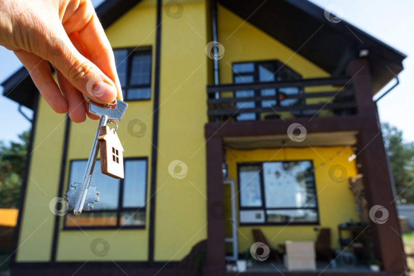 Скачать Ключ от дома с крошечным домиком в руках владельца рядом с коттеджем - продажа, переезд, бронирование, проект коттеджа, ипотека, страхование жилья и недвижимости. фотосток Ozero