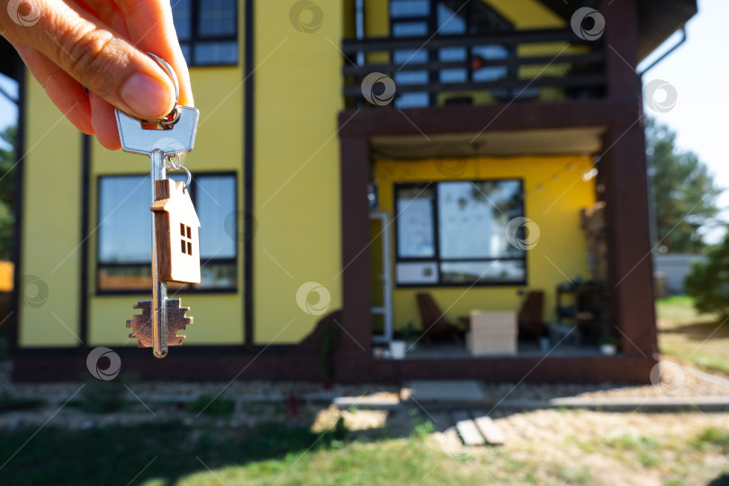 Скачать Ключ от дома с крошечным домиком в руках владельца рядом с коттеджем - продажа, переезд, бронирование, проект коттеджа, ипотека, страхование жилья и недвижимости. фотосток Ozero