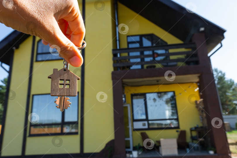 Скачать Ключ от дома с крошечным домиком в руках владельца рядом с коттеджем - продажа, переезд, бронирование, проект коттеджа, ипотека, страхование жилья и недвижимости. фотосток Ozero