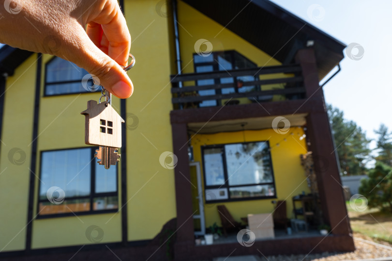 Скачать Ключ от дома с крошечным домиком в руках владельца рядом с коттеджем - продажа, переезд, бронирование, проект коттеджа, ипотека, страхование жилья и недвижимости. фотосток Ozero