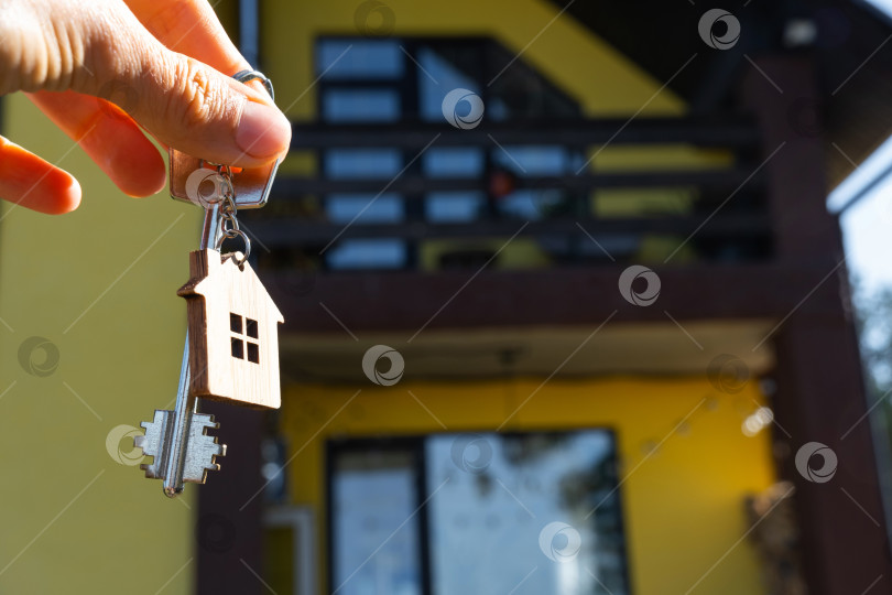 Скачать Ключ от дома с крошечным домиком в руках владельца рядом с коттеджем - продажа, переезд, бронирование, проект коттеджа, ипотека, страхование жилья и недвижимости. фотосток Ozero