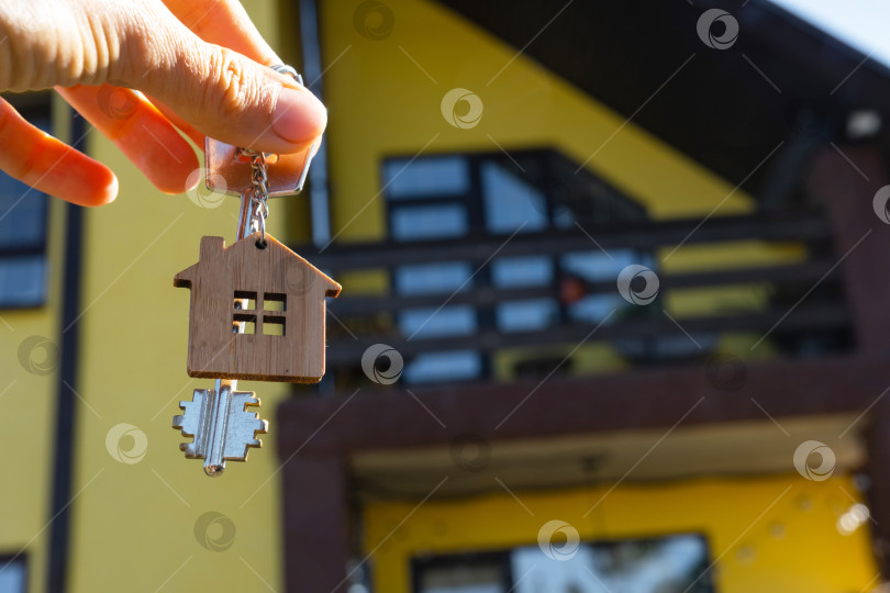 Скачать Ключ от дома с крошечным домиком в руках владельца рядом с коттеджем - продажа, переезд, бронирование, проект коттеджа, ипотека, страхование жилья и недвижимости. фотосток Ozero