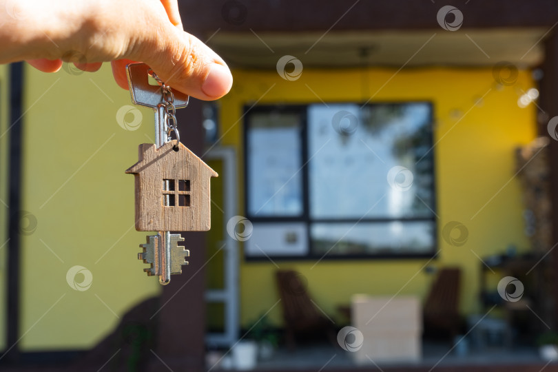 Скачать Ключ от дома с крошечным домиком в руках владельца рядом с коттеджем - продажа, переезд, бронирование, проект коттеджа, ипотека, страхование жилья и недвижимости. фотосток Ozero