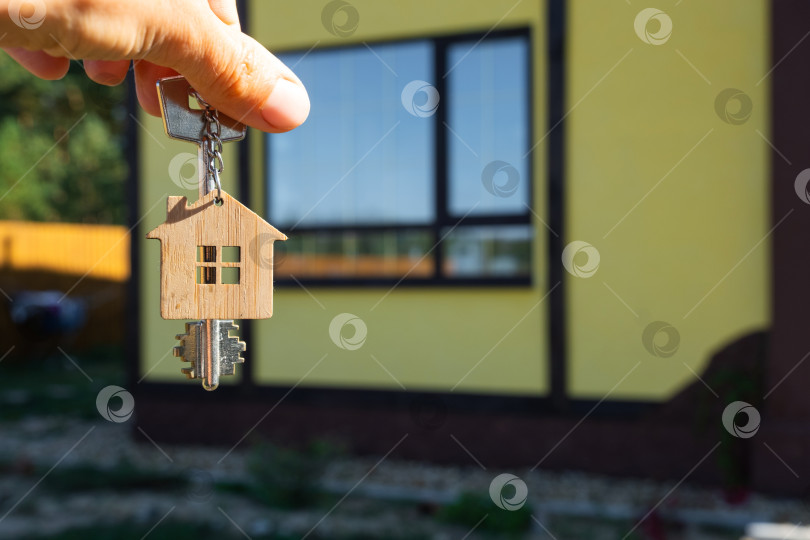Скачать Ключ от дома с крошечным домиком в руках владельца рядом с коттеджем - продажа, переезд, бронирование, проект коттеджа, ипотека, страхование жилья и недвижимости. фотосток Ozero