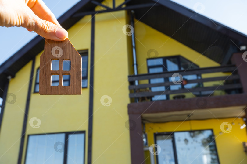 Скачать Ключ от дома с крошечным домиком в руках владельца рядом с коттеджем - продажа, переезд, бронирование, проект коттеджа, ипотека, страхование жилья и недвижимости. фотосток Ozero