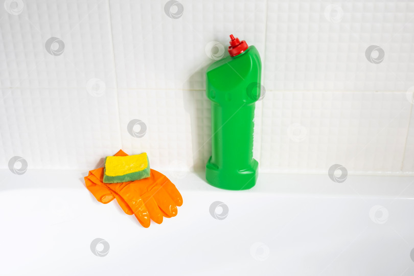 Скачать Крупным планом бутылка с моющим средством в ванной комнате дома, губка для мытья посуды и резиновые перчатки на ванной. Наведение порядка, чистоты и гигиены в доме, услуги по уборке фотосток Ozero