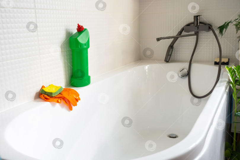 Скачать Крупным планом бутылка с моющим средством в ванной комнате дома, губка для мытья посуды и резиновые перчатки на ванной. Наведение порядка, чистоты и гигиены в доме, услуги по уборке фотосток Ozero
