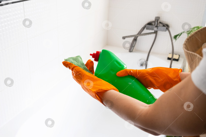 Скачать Руки в резиновых перчатках крупным планом и бутылка с моющим средством в ванной комнате дома, губка для мытья посуды и чистящее средство на ванне. Наведение порядка, чистоты и гигиены в доме, услуги по уборке фотосток Ozero