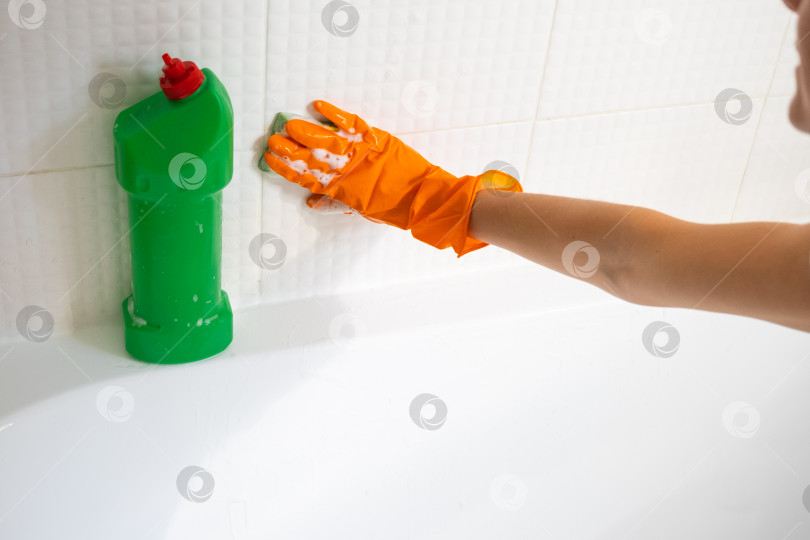 Скачать Руки в резиновых перчатках крупным планом и бутылка с моющим средством в ванной комнате дома, губка для мытья посуды и чистящее средство на ванне. Наведение порядка, чистоты и гигиены в доме, услуги по уборке фотосток Ozero