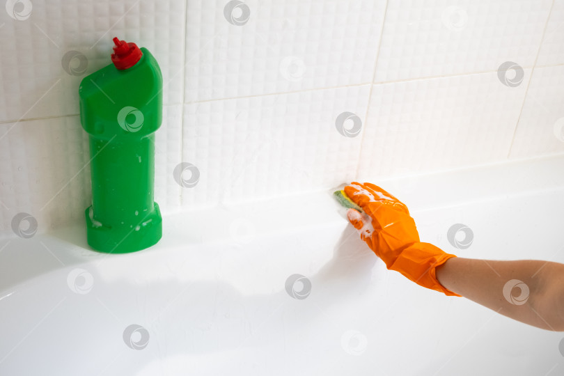 Скачать Руки в резиновых перчатках крупным планом и бутылка с моющим средством в ванной комнате дома, губка для мытья посуды и чистящее средство на ванне. Наведение порядка, чистоты и гигиены в доме, услуги по уборке фотосток Ozero