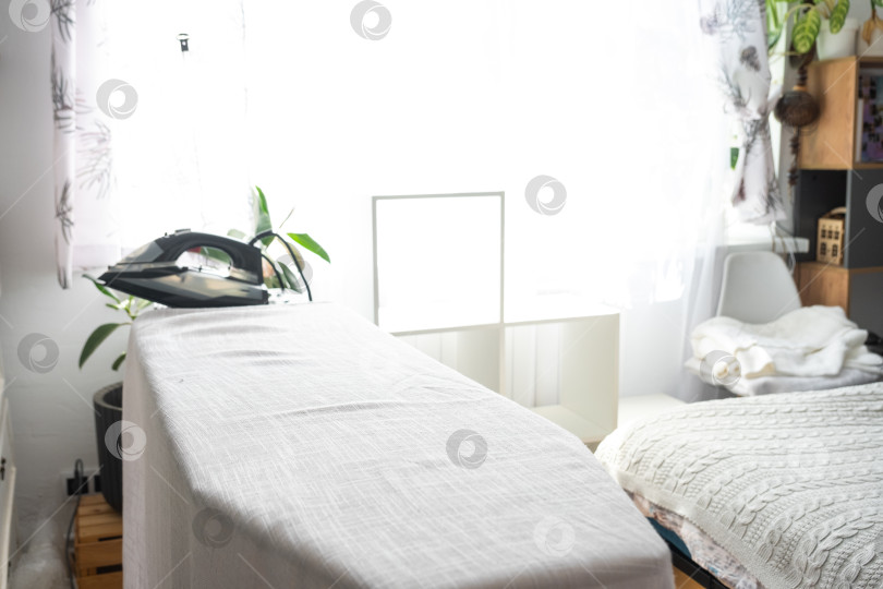 Скачать Утюг находится на гладильной доске с обычной тканью в комнате. фотосток Ozero