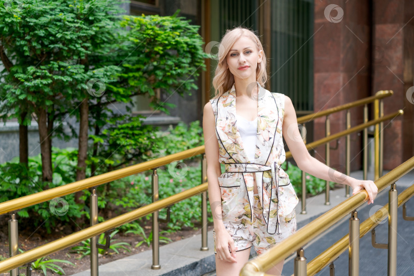 Скачать Женщина в цветастом платье и белом топе стоит на тротуаре фотосток Ozero