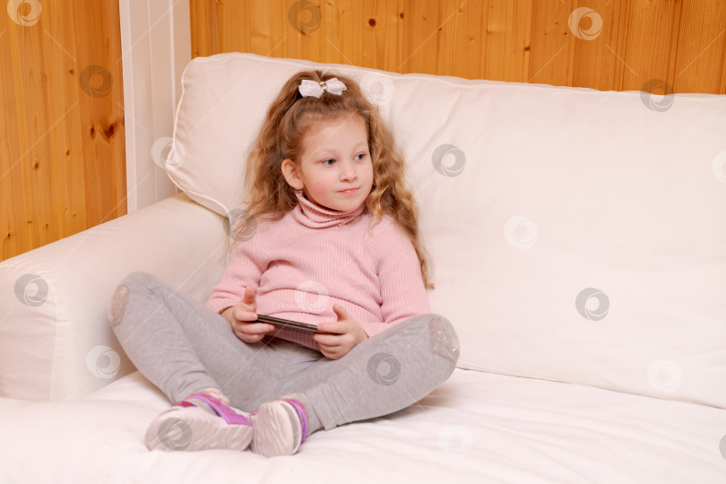 Скачать Маленькая девочка сидит на диване и играет в видеоигру фотосток Ozero