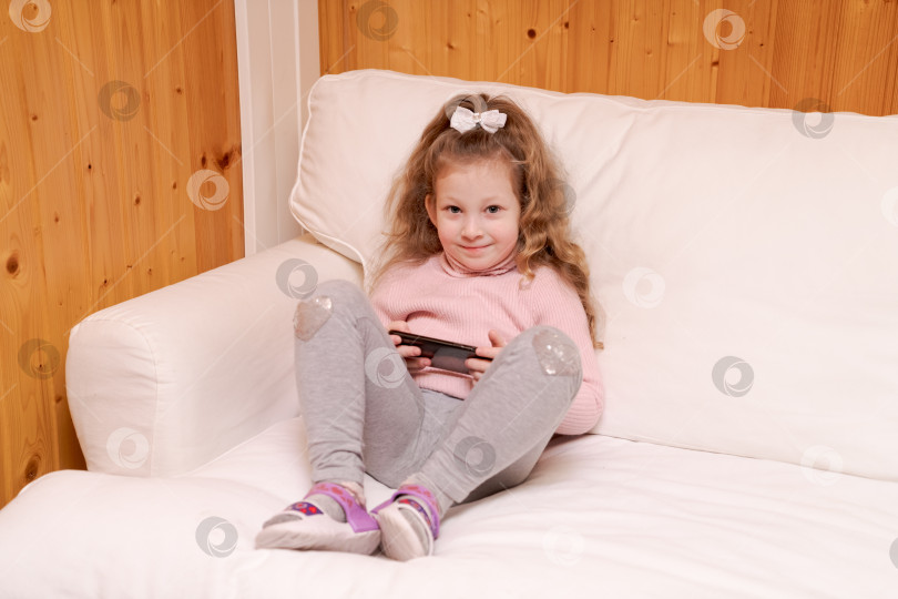 Скачать Маленькая девочка сидит на диване и играет в видеоигру фотосток Ozero