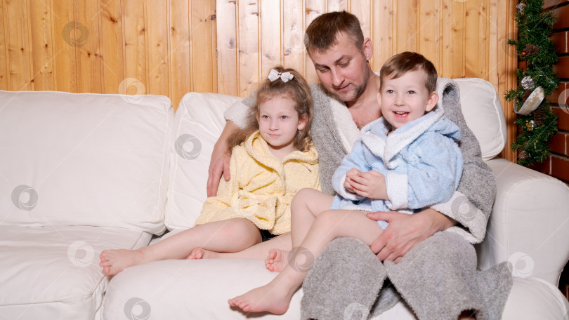 Скачать Мужчина сидит на диване с двумя детьми фотосток Ozero