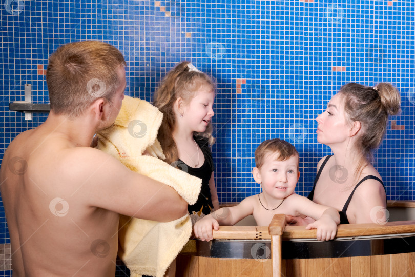 Скачать Мужчина держит в руках полотенце, в то время как женщина и двое детей находятся в ванне фотосток Ozero