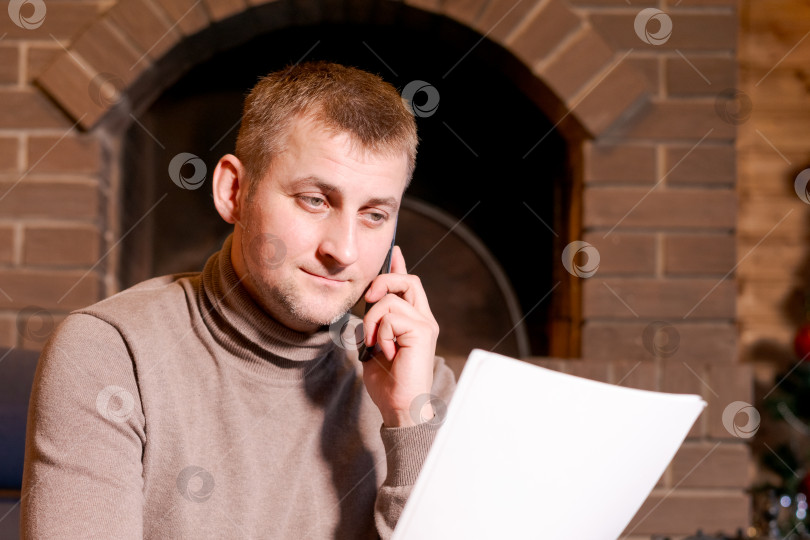 Скачать Мужчина разговаривает по мобильному телефону, глядя на лист бумаги фотосток Ozero