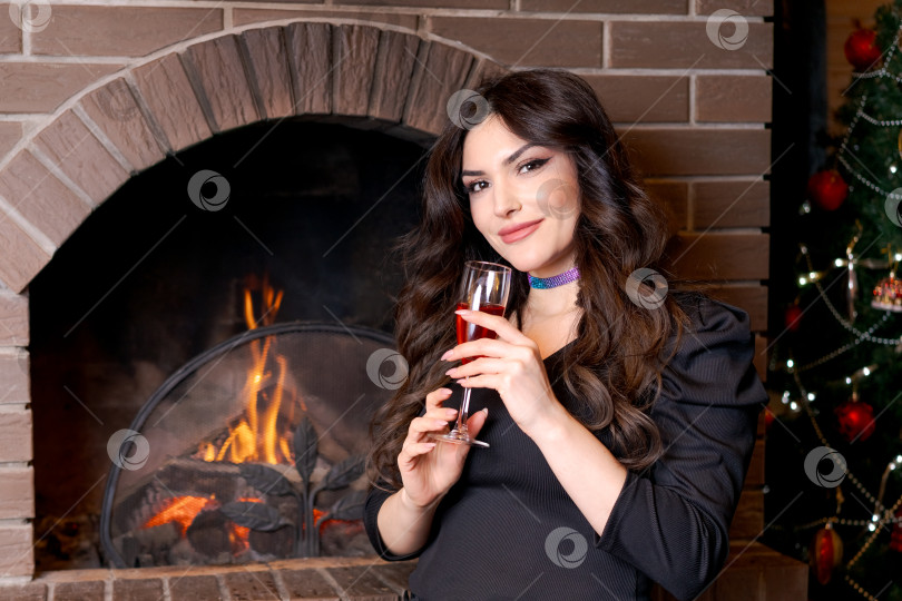Скачать Женщина стоит с бокалом вина в руках перед камином фотосток Ozero