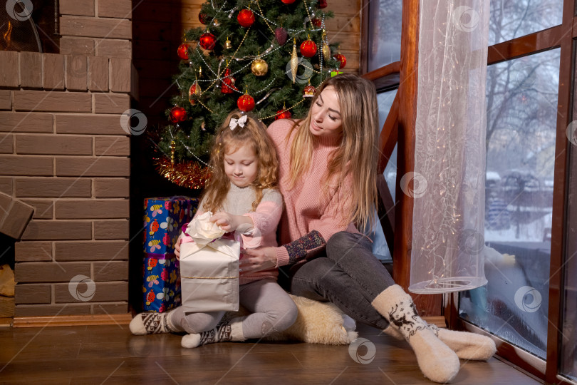 Скачать Женщина и ребенок сидят на полу перед рождественской елкой фотосток Ozero