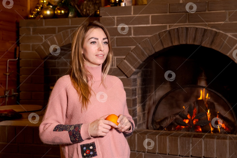 Скачать Женщина стоит перед камином, держа в руках апельсин. фотосток Ozero