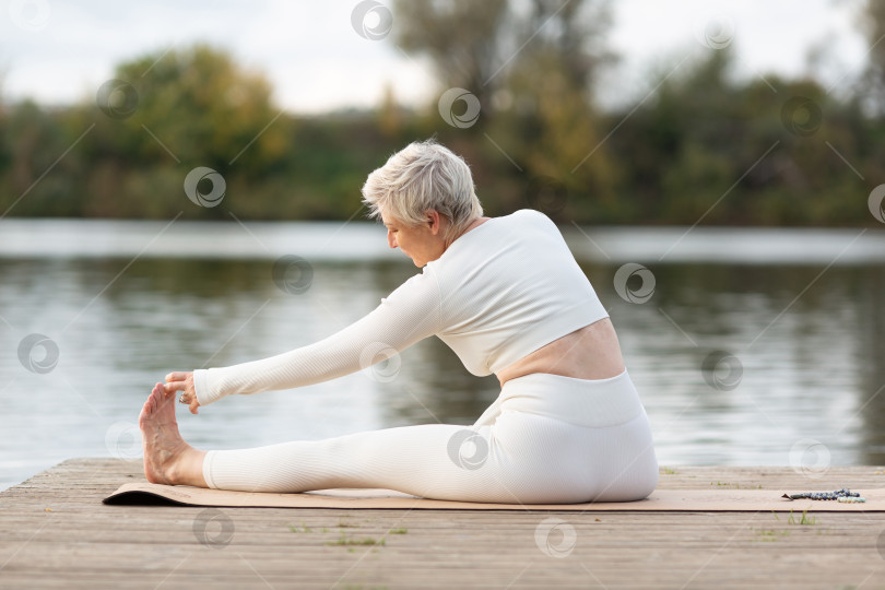 Скачать Взрослая женщина занимается йогой на природе у воды фотосток Ozero