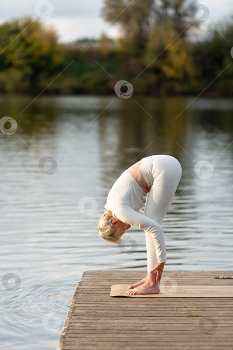 Скачать Взрослая женщина занимается йогой на природе у воды фотосток Ozero