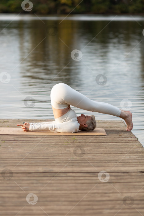 Скачать Взрослая женщина занимается йогой на природе у воды фотосток Ozero