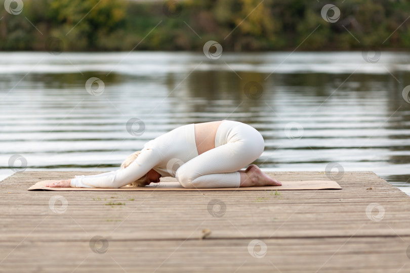 Скачать Взрослая женщина занимается йогой на природе у воды фотосток Ozero