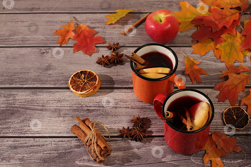 Скачать Сезонная абстрактная композиция с эмалированными кружками с горячим осенним напитком, глинтвейном с яблоками и опавшими листьями, бадьяном и корицей, баннер для экрана, концепция осеннего поздравления, макет меню. фотосток Ozero