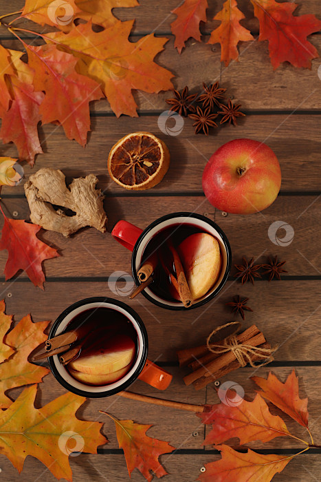 Скачать Сезонная абстрактная композиция с эмалированными кружками с горячим осенним напитком, глинтвейном с яблоками и опавшими листьями, бадьяном и корицей, баннер для экрана, концепция осеннего поздравления, макет меню. фотосток Ozero