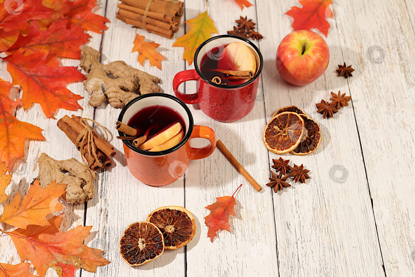 Скачать Сезонная абстрактная композиция с эмалированными кружками с горячим осенним напитком, глинтвейном с яблоками и опавшими листьями, бадьяном и корицей, баннер для экрана, концепция осеннего поздравления, макет меню. фотосток Ozero