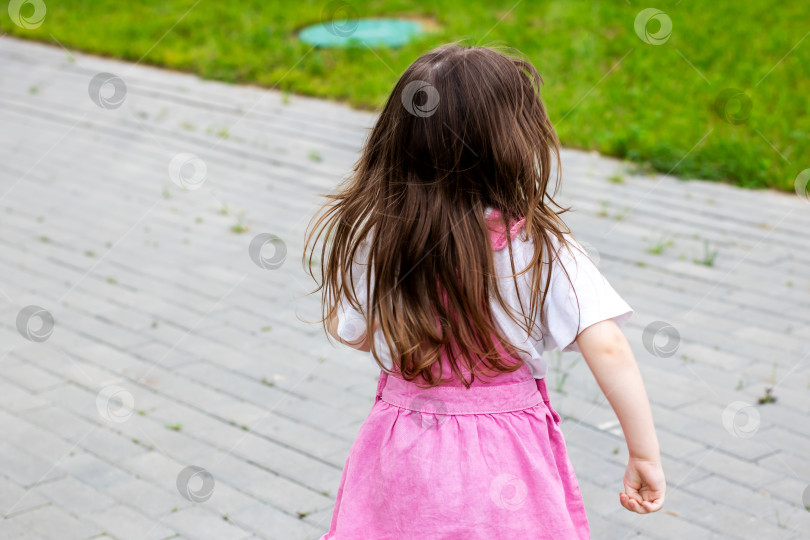Скачать Маленькая девочка в розовом платьице радостно идет по тротуару фотосток Ozero