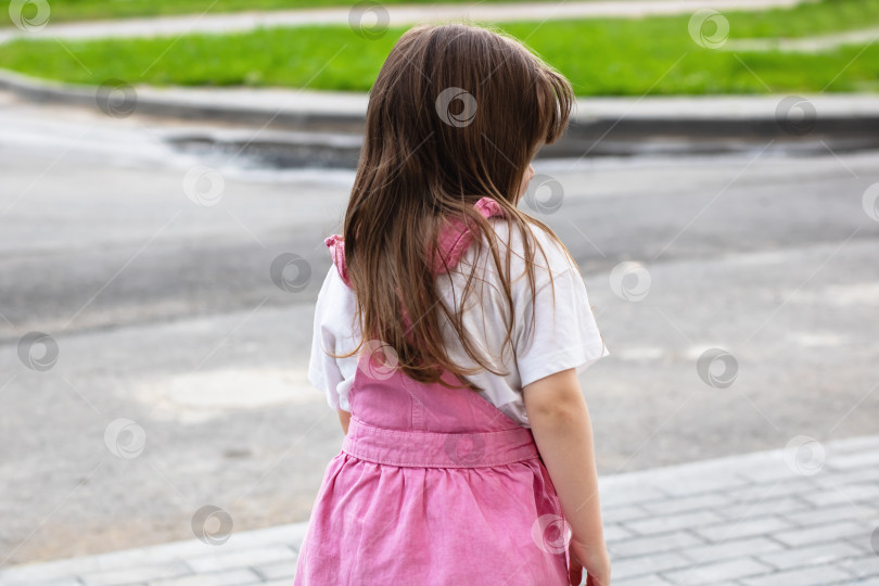 Скачать Маленькая девочка в розовом платьице радостно стоит на тротуаре фотосток Ozero