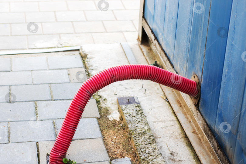 Скачать Красный гофрированный шланг выходит из Синей металлической стены на городском тротуаре фотосток Ozero